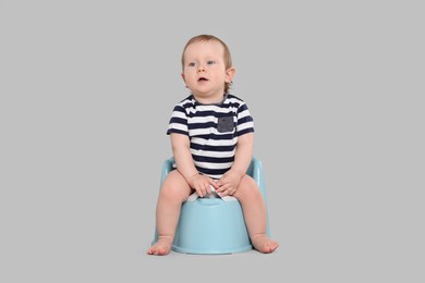 Photo of Little child sitting on baby potty against light grey background