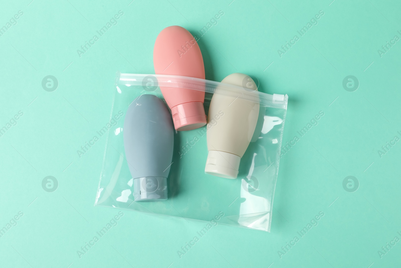 Photo of Cosmetic travel kit in plastic bag on turquoise background, top view. Bath accessories