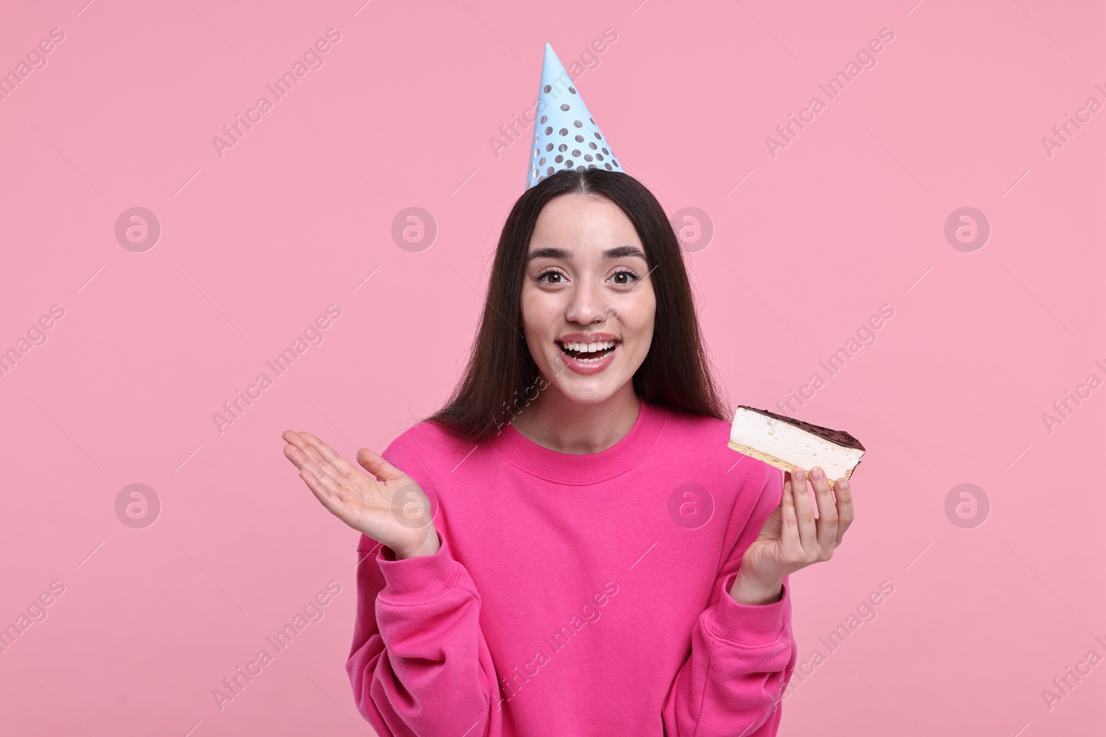 Photo of Woman in party hat with piece of tasty cake on pink background