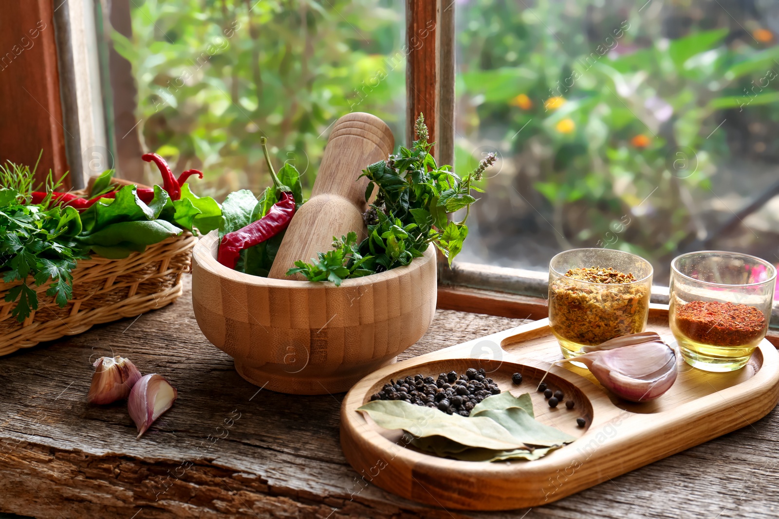 Photo of Mortar with pestle, fresh green herbs and different spices on wooden table near window