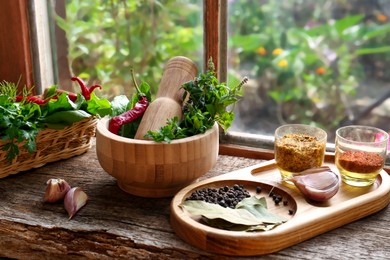 Photo of Mortar with pestle, fresh green herbs and different spices on wooden table near window