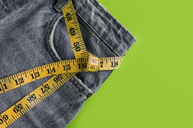 Photo of Jeans and measuring tape on green background, top view with space for text. Weight loss concept