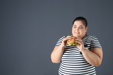 Photo of Overweight woman with hamburger and space for text on gray background