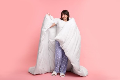 Happy woman in pyjama wrapped in blanket on pink background