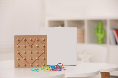 Photo of Wooden geoboard with rubber bands on white table indoors. Educational toy for motor skills development