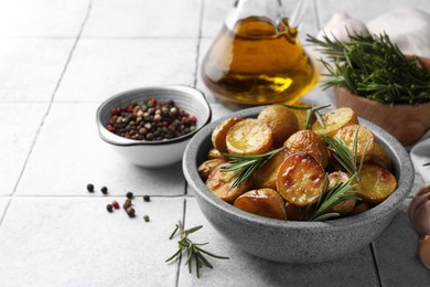 Photo of Bowl with tasty baked potato and aromatic rosemary on white tiled table. Space for text