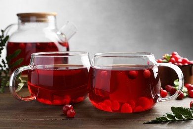 Photo of Tasty hot cranberry tea in glasses and fresh berries on wooden table
