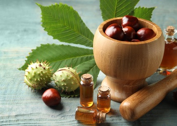 Mortar with pestle, chestnuts and bottles of essential oil on blue wooden table