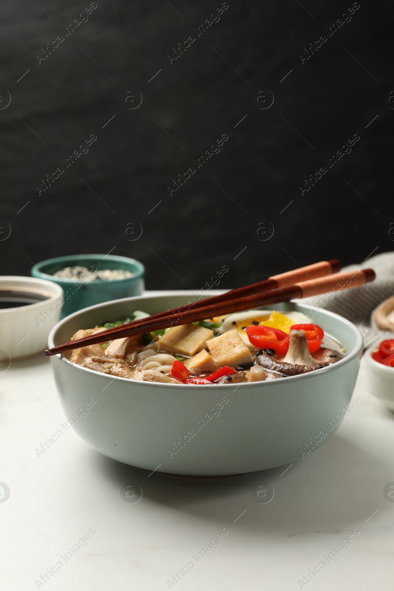 Photo of Bowl of delicious ramen, ingredients and chopsticks on white table, closeup. Noodle soup