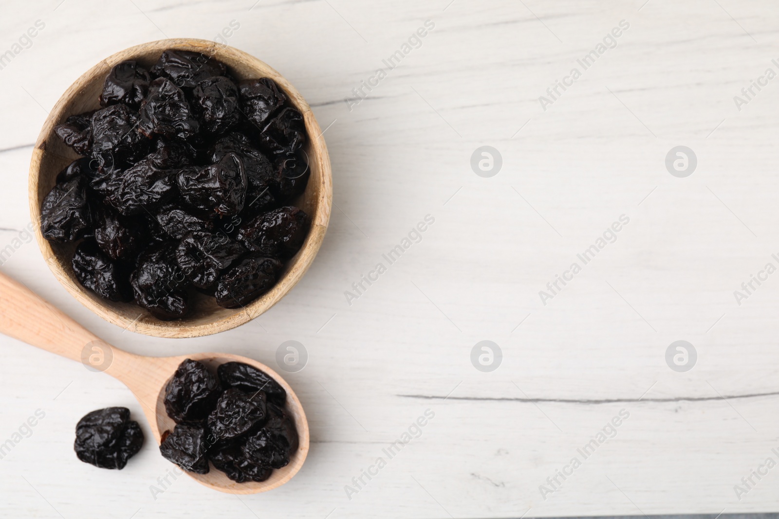 Photo of Bowl and spoon with sweet dried prunes on white wooden table, flat lay. Space for text