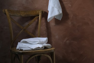 Photo of White terry towels on wooden chair against brown background. Space for text