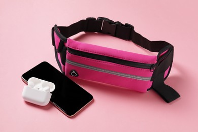 Photo of Stylish waist bag with smartphone and earphones on pink background