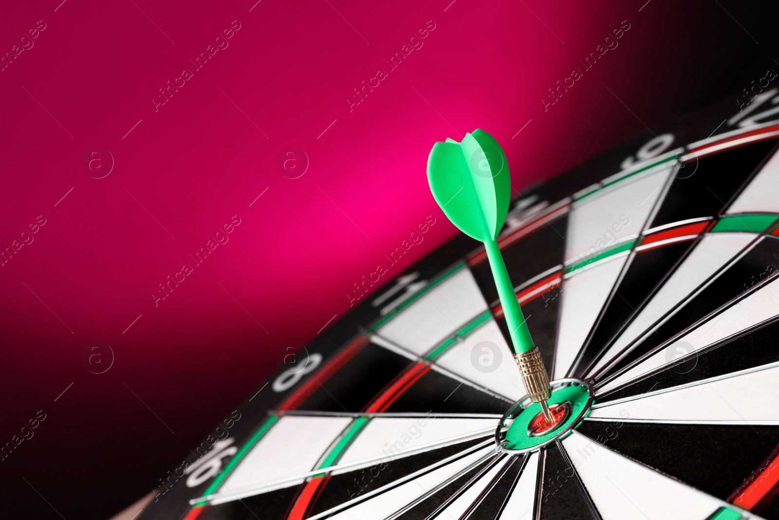 Photo of Green arrow hitting target on dart board against magenta background. Space for text