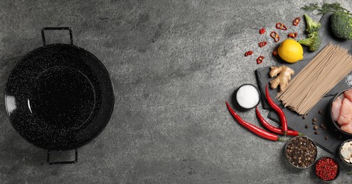 Photo of Empty iron wok and raw ingredients on grey table, flat lay. Space for text