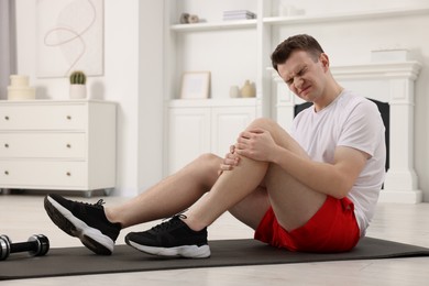Man suffering from leg pain on mat at home
