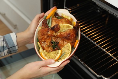 Photo of Woman taking baked chicken with orange slices out of oven, closeup