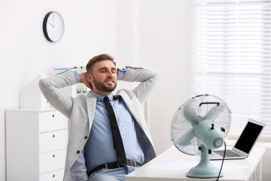 Photo of Man enjoying air flow from fan at workplace