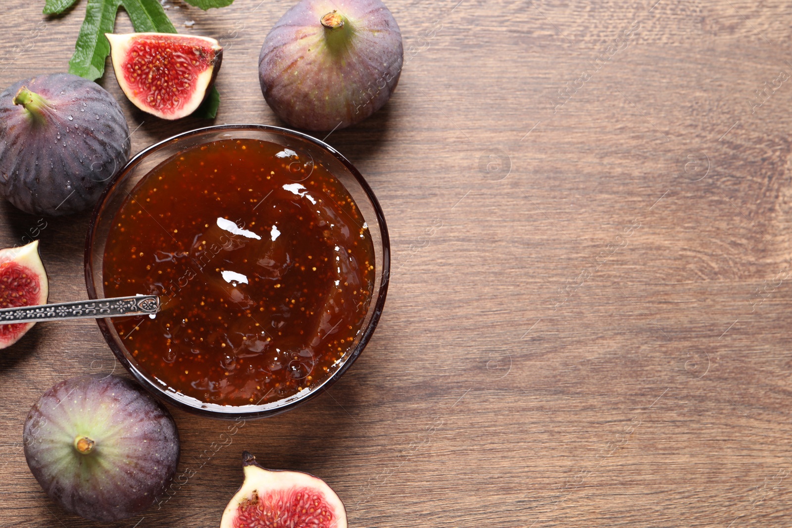 Photo of Glass bowl with tasty sweet jam and fresh figs on wooden table, flat lay. Space for text