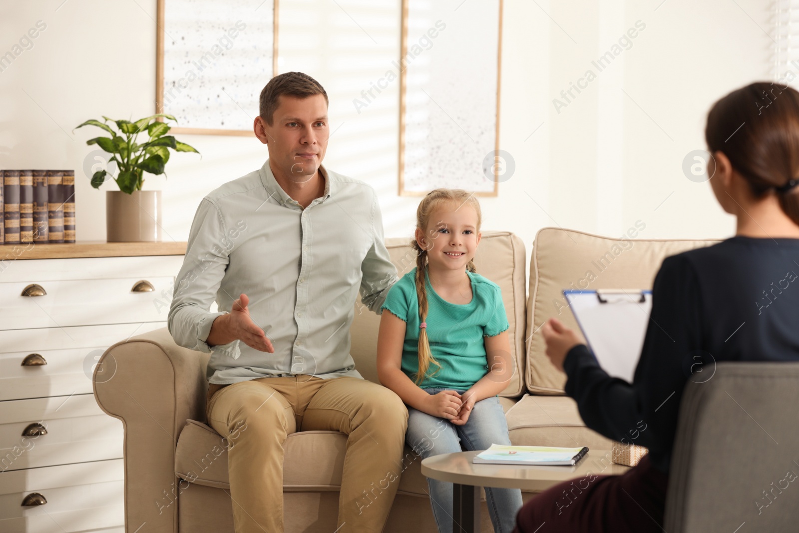 Photo of Little girl and her father on appointment with child psychotherapist indoors