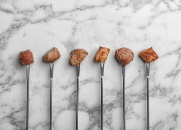 Photo of Forks with fried meat fondue pieces on marble background, top view