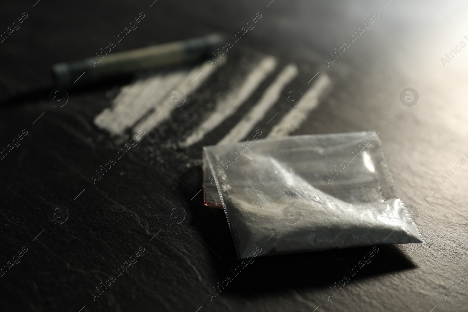 Photo of Drug addiction. Plastic bag with cocaine and rolled dollar banknote on grey textured table, selective focus