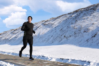 Photo of Happy man running past snowy hill in winter. Outdoors sports exercises