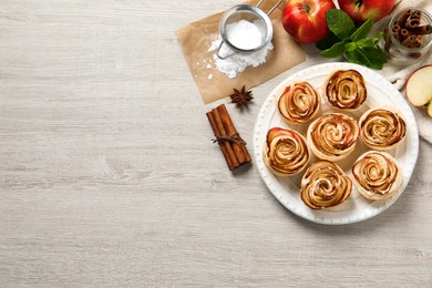 Photo of Freshly baked apple roses on white wooden table, flat lay. Space for text