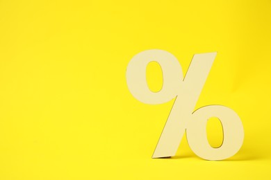 Photo of Wooden percent sign on yellow background. Space for text