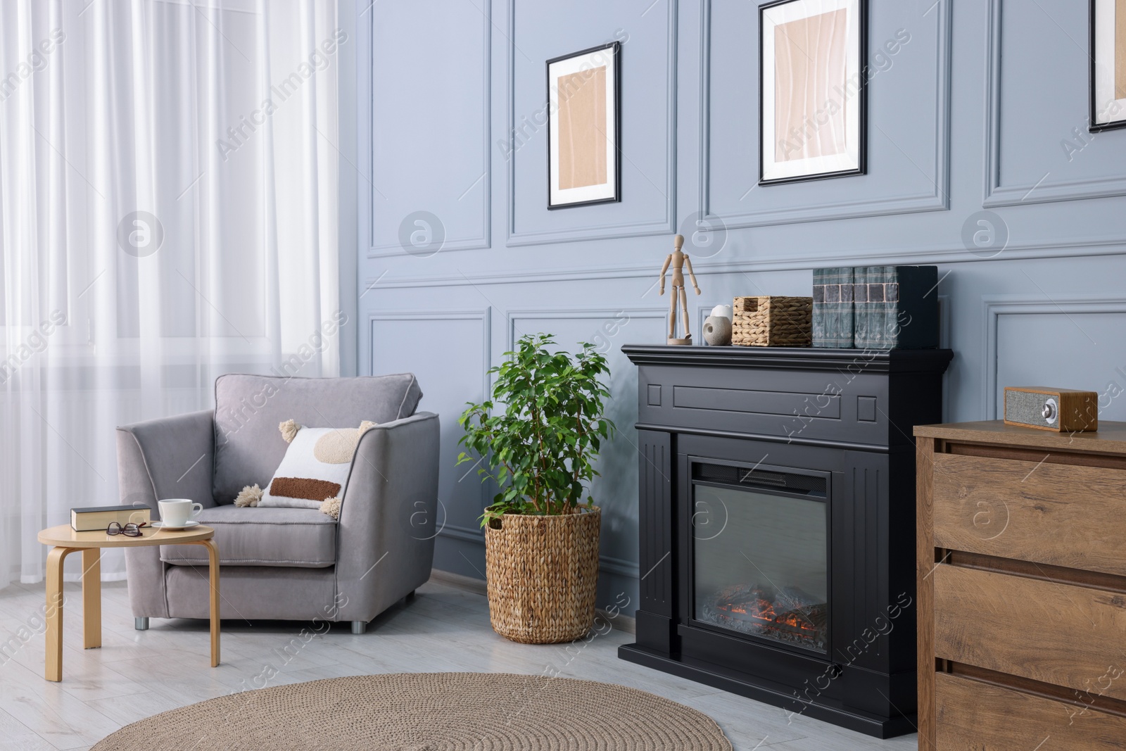 Photo of Black stylish fireplace near potted plant and armchair in cosy living room