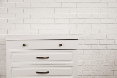 Photo of Modern chest of drawers near white brick wall. Space for text