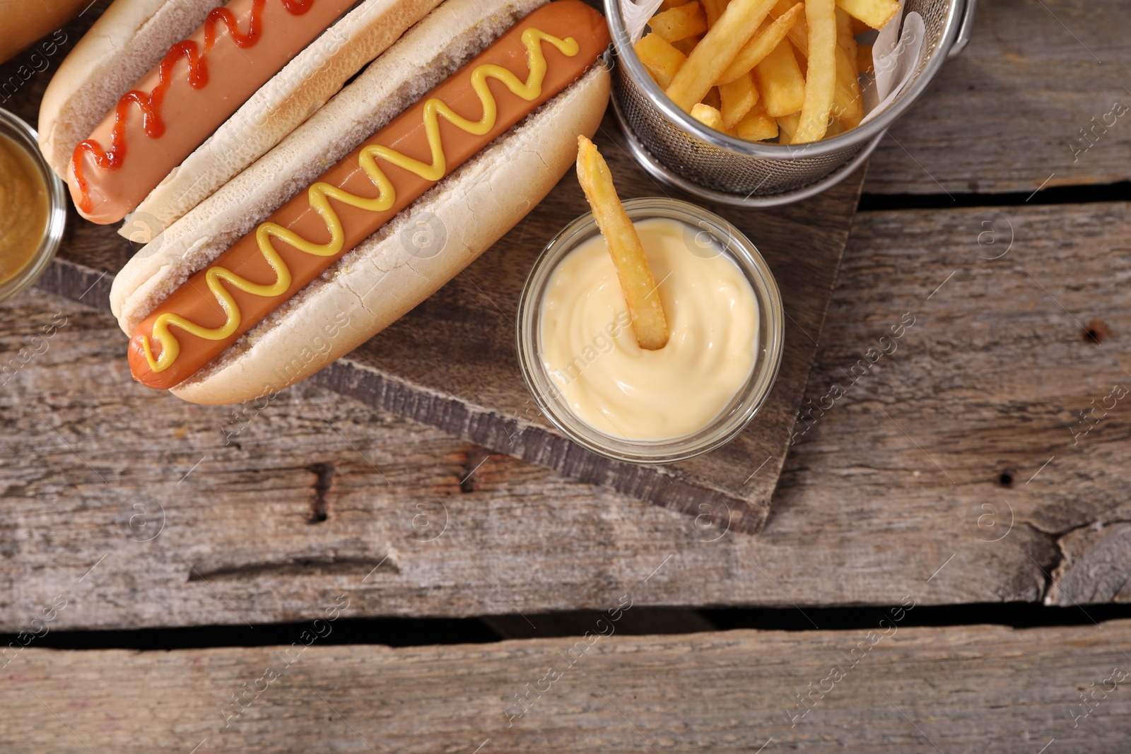 Photo of Delicious hot dogs with sauces and French fries on wooden table, top view. Space for text