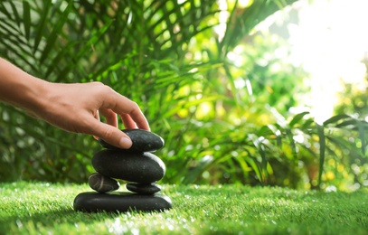 Photo of Woman stacking stones on green grass in garden, closeup. Space for text