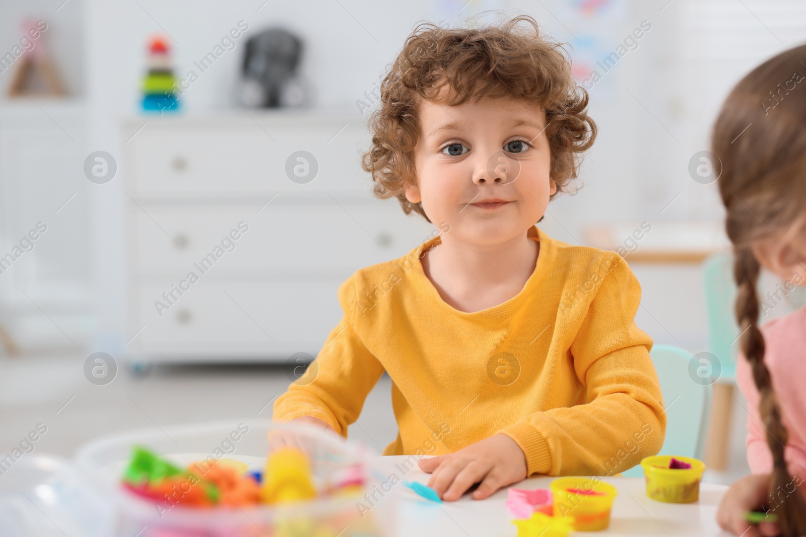 Photo of Little children modeling from plasticine at white table in kindergarten. Space for text