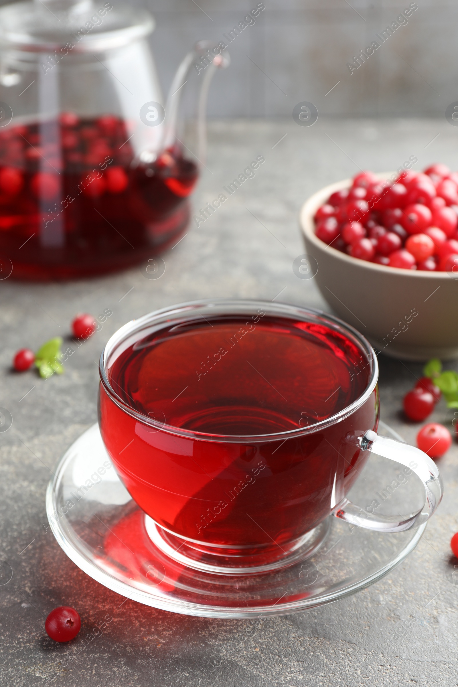 Photo of Tasty hot cranberry tea in glass cup and fresh berries on light grey textured table