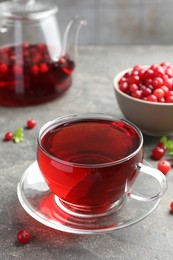 Tasty hot cranberry tea in glass cup and fresh berries on light grey textured table