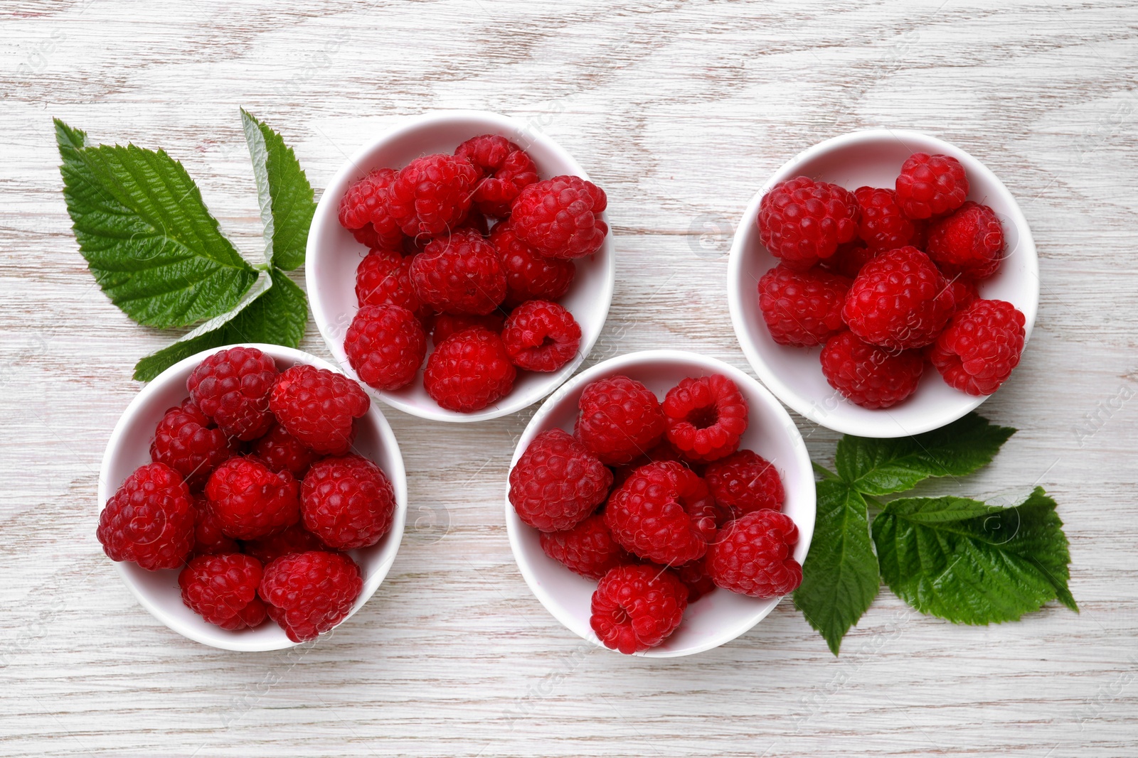 Photo of Tasty ripe raspberries and green leaves on white wooden table, flat lay