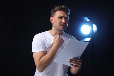 Casting call. Emotional man with script performing on black background