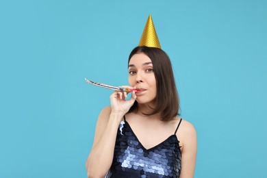Photo of Happy young woman in party hat with blower on light blue background