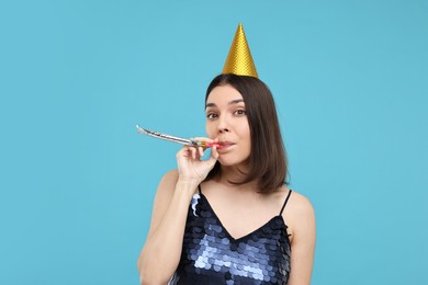 Happy young woman in party hat with blower on light blue background