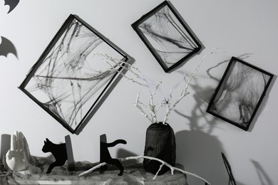 Photo of Black frames with cobweb on white wall and different Halloween decor on fireplace indoors