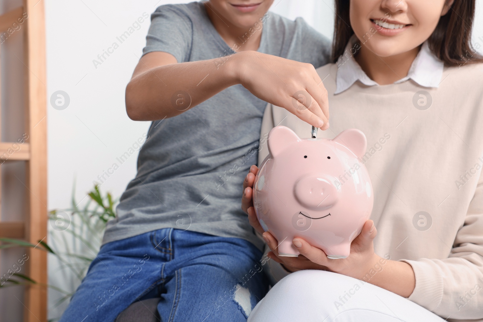 Photo of Boy with his mother putting money into piggy bank at home, closeup