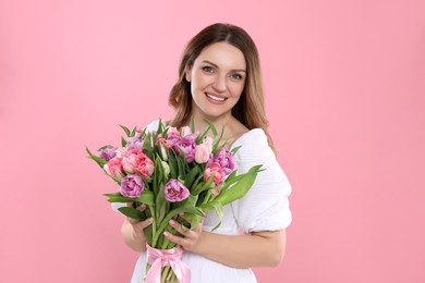 Happy young woman with bouquet of beautiful tulips on pink background