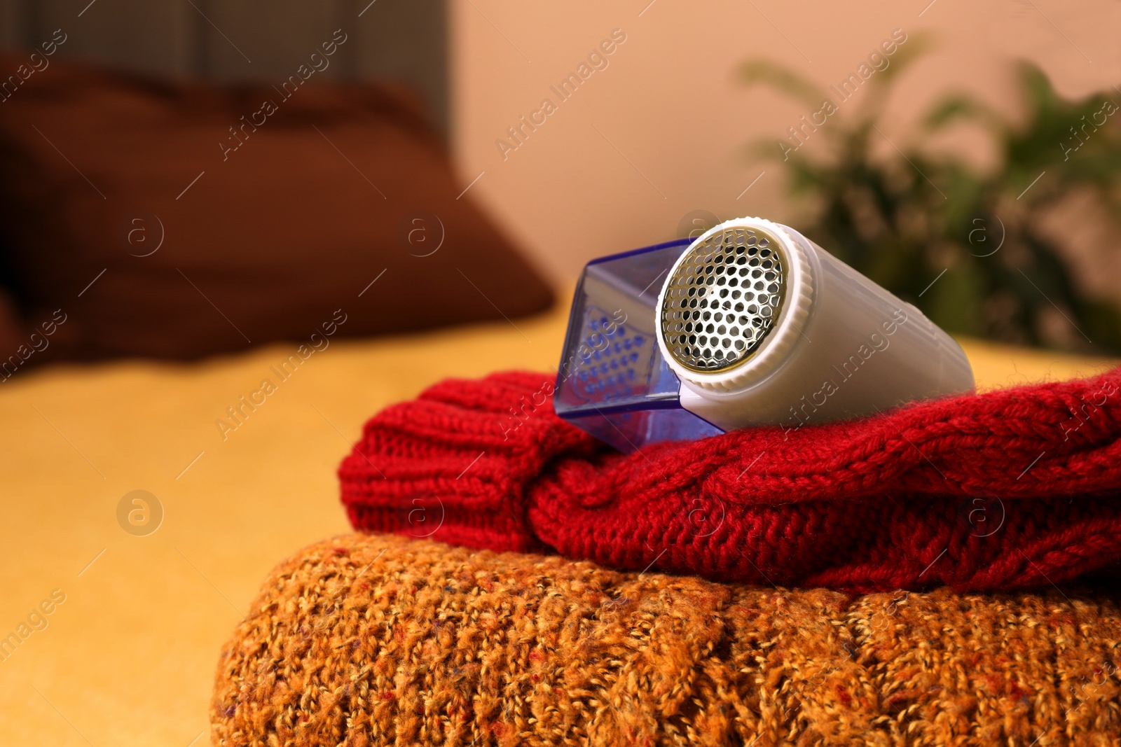 Photo of Modern fabric shaver and knitted clothes on bed indoors, closeup