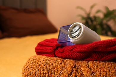 Photo of Modern fabric shaver and knitted clothes on bed indoors, closeup