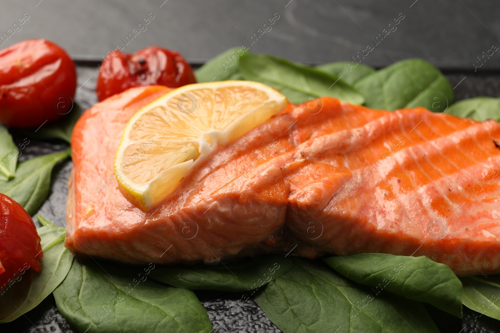 Photo of Tasty grilled salmon with tomatoes, lemon and spinach on table, closeup