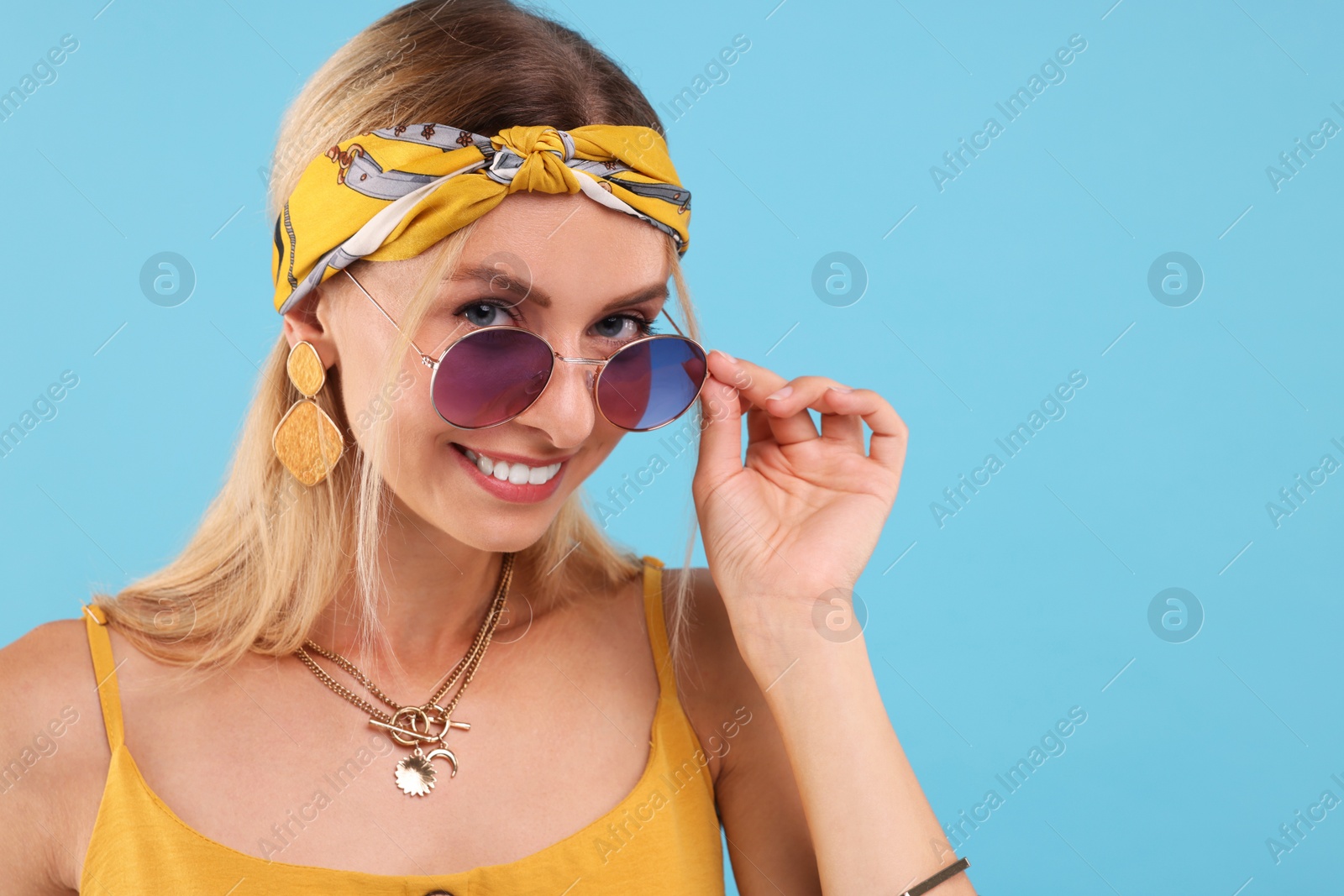 Photo of Portrait of smiling hippie woman in sunglasses on light blue background. Space for text