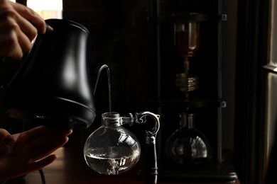 Barista pouring water into vacuum coffee maker at table in cafe, closeup