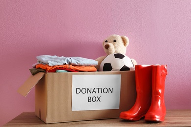Donation box with clothes and toys on table against color background
