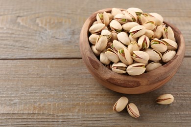 Photo of Delicious pistachios in bowl on wooden table. Space for text