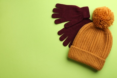 Woolen gloves and hat on green background, flat lay. Space for text